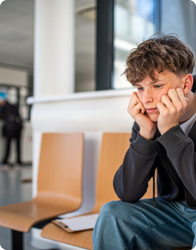 Anxiety - Boy sitting down on a chair, hands on his face, elbows resting on his knees as he looks on in anxiousness.
