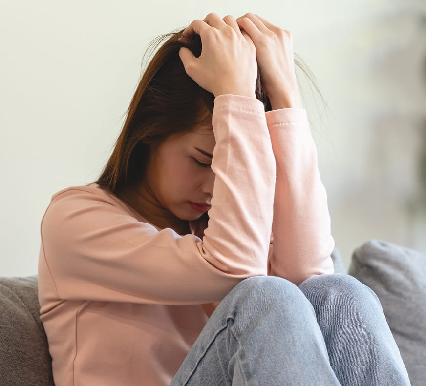 an anxious girl covering her face with his arms and hands on her head as she sits down
