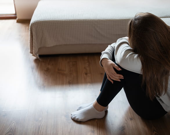 Signs of Suicidal Ideation - Girl on the floor with head buried in her arms with her knees up.