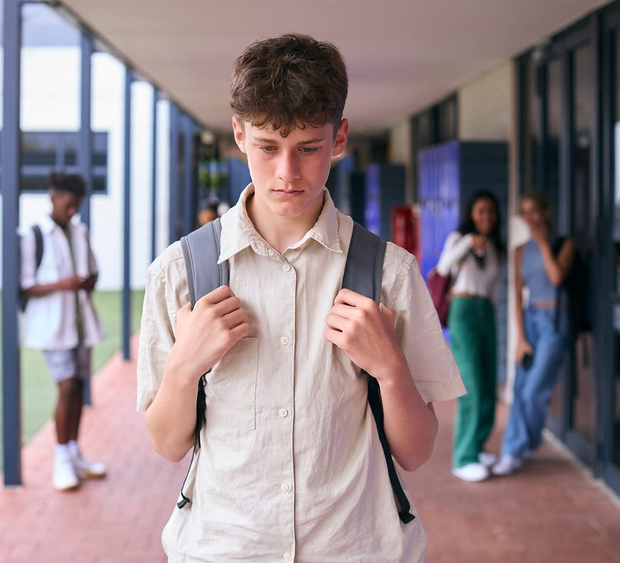 Bullying & Victimization - Boy walking away from some laughing teens at a school as he looks down in sadness.