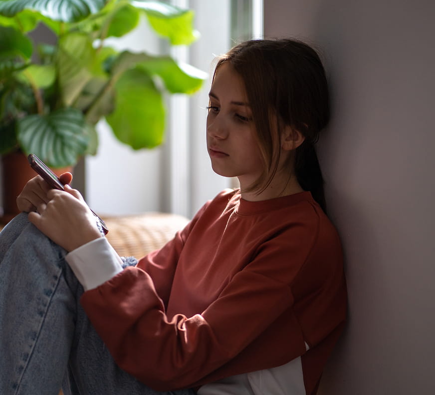 a girl sitting in the dark with her phone as she looks onward, potentially suffering from depression.