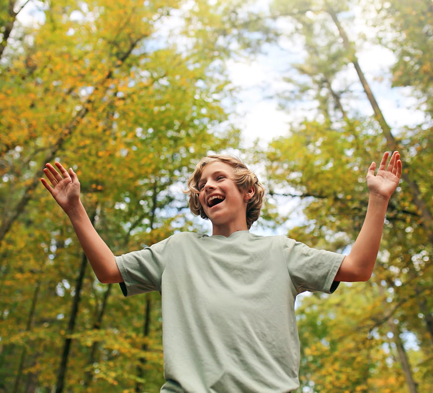 smiling teen in the forest with his hands up