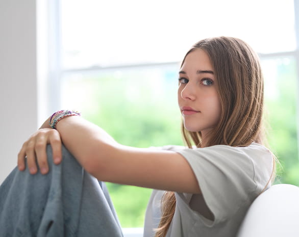 girl sitting by a window, holding her knees and looking a bit off.