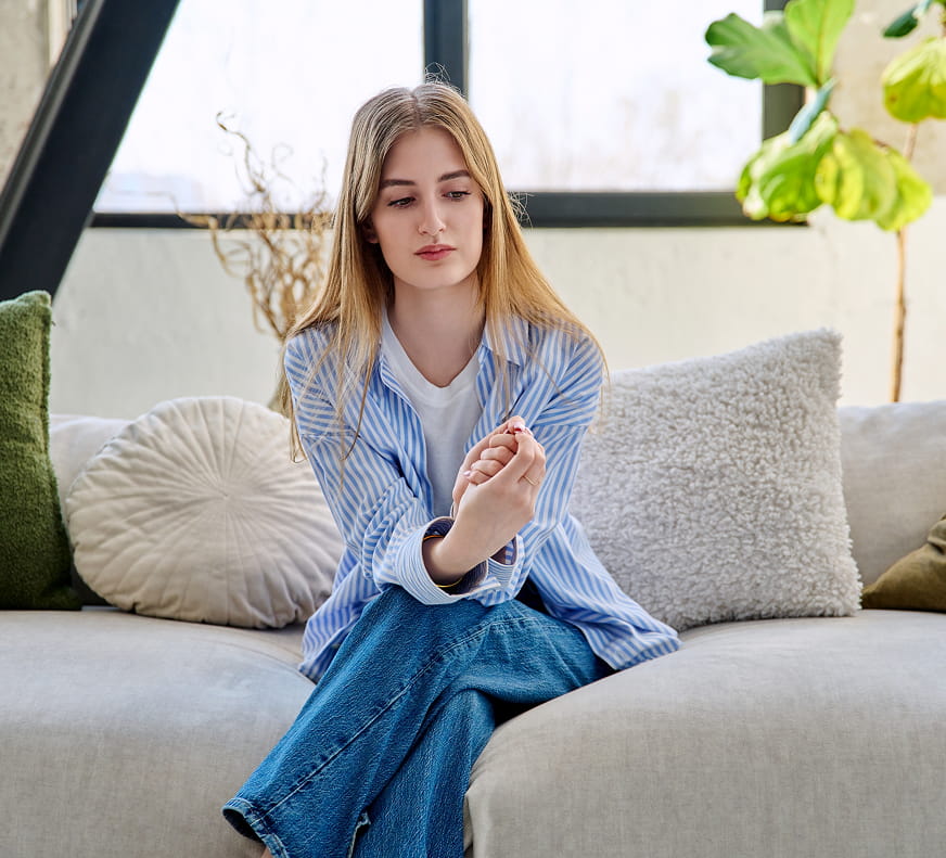 Self-Harm Treatment for Teens - Girl sitting on a couch with her legs crossed, looking on in sadness.