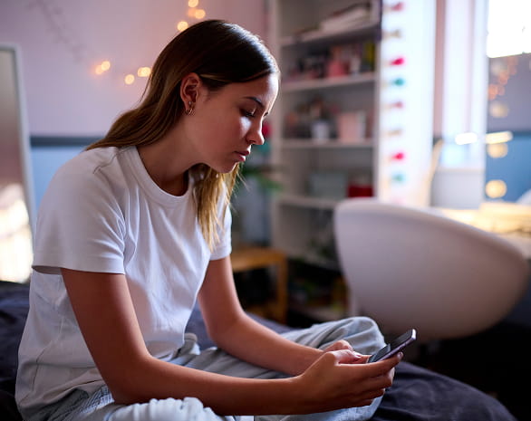 Signs of Anxiety - Girl sitting cross-legged in her room starting at her phone.