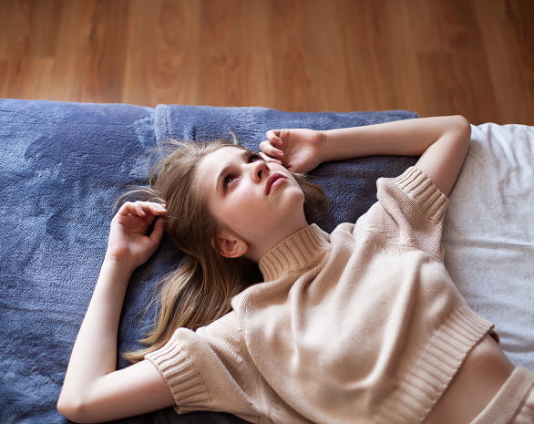 Girl laying on her bed staring at the ceiling in distress.