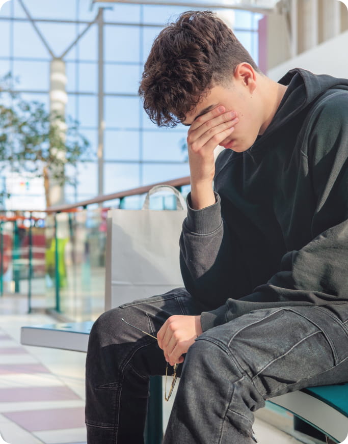 boy who has taken his glasses off as he buries his face in his hand, distressed about something.
