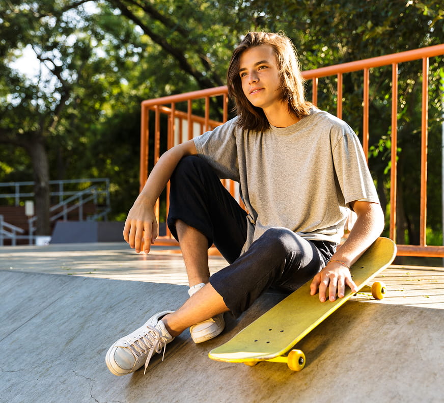 boy sitting down with his skateboard at a skatepark looking off in the distance.