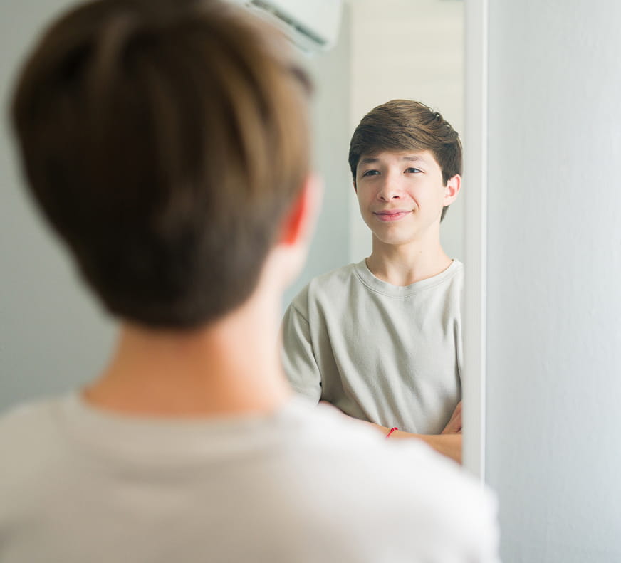 a boy proudly looking at himself in the mirror, smiling and crossing his arms